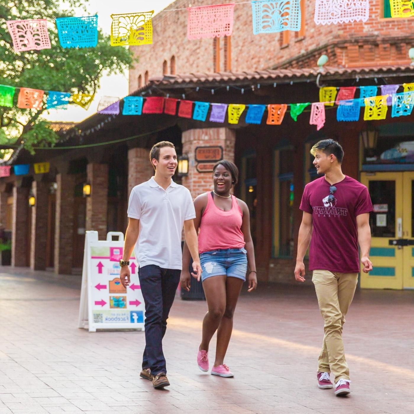 three 澳门威尼斯人 students walk through Market Square under papel picado
